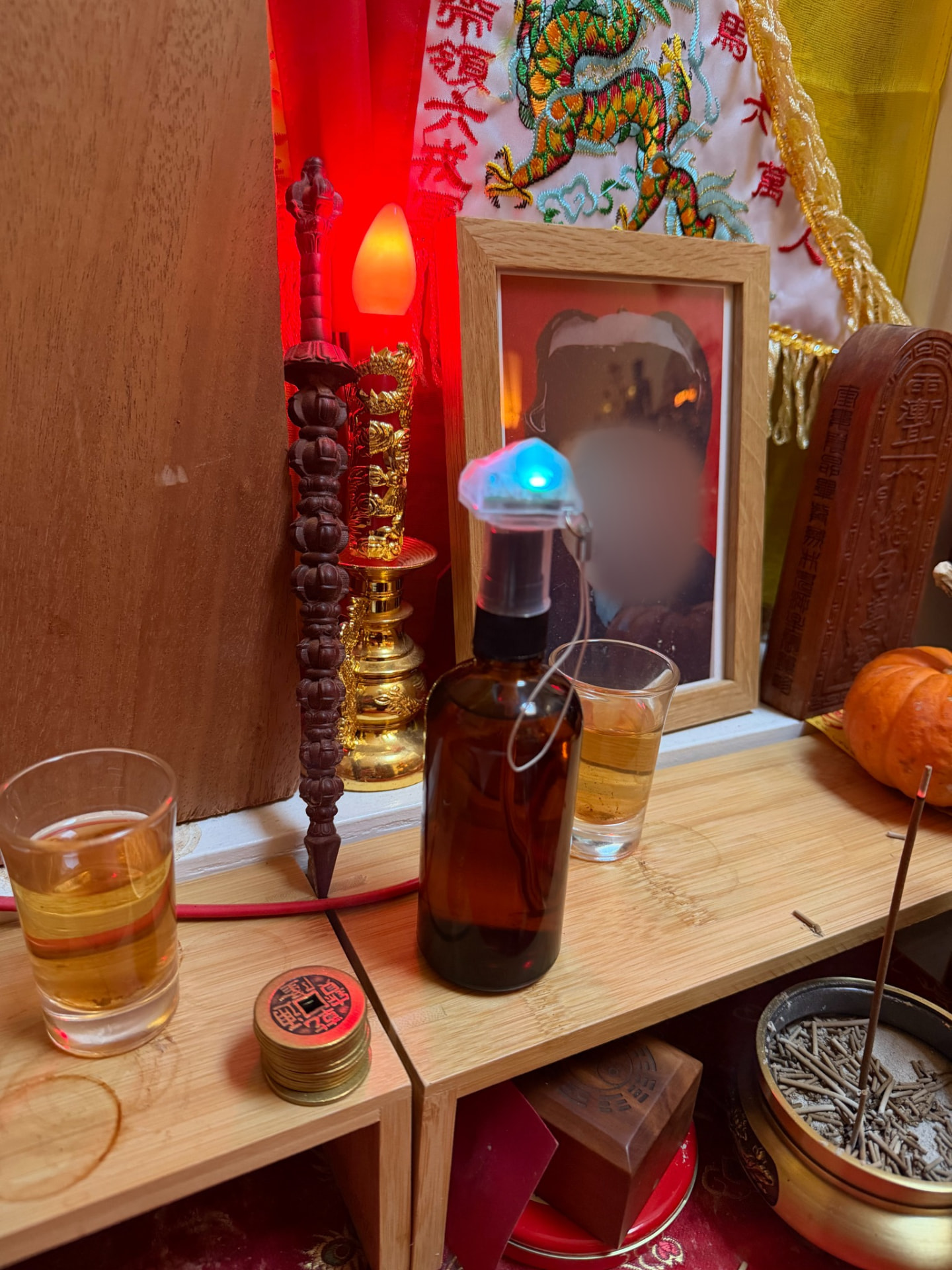 Authentic Daoist ritual altar with an amber Jow bottle, offerings, illuminated ritual object, and a framed portrait with face obscured